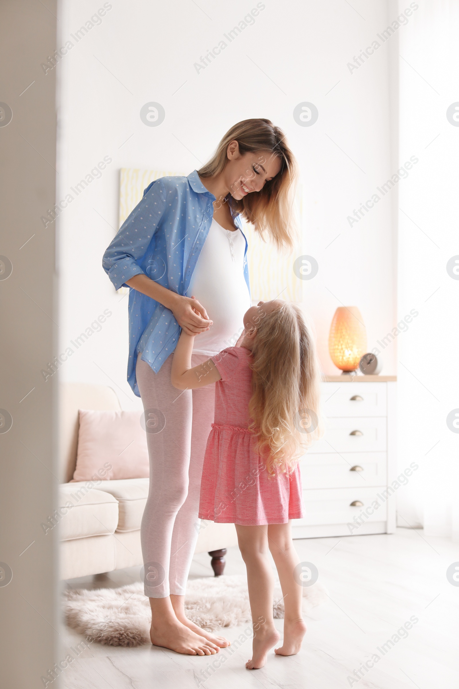 Photo of Young pregnant woman with cute daughter at home