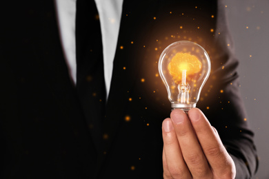 Image of Man holding light bulb with shining brain inside against grey background, closeup. Idea generation