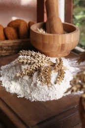 Photo of Pile of wheat flour and spikes on wooden table indoors