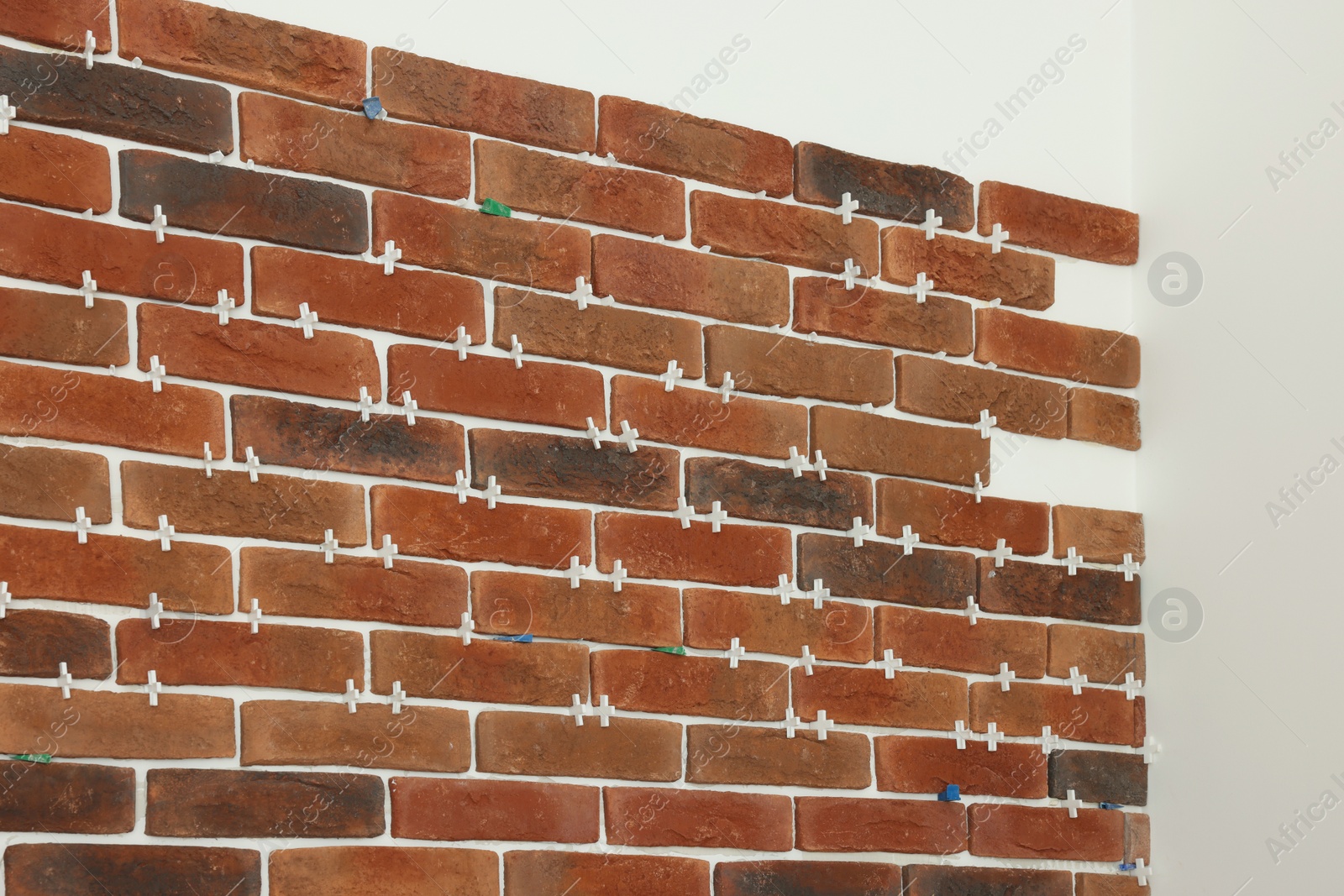 Photo of Decorative bricks with tile leveling system on white wall