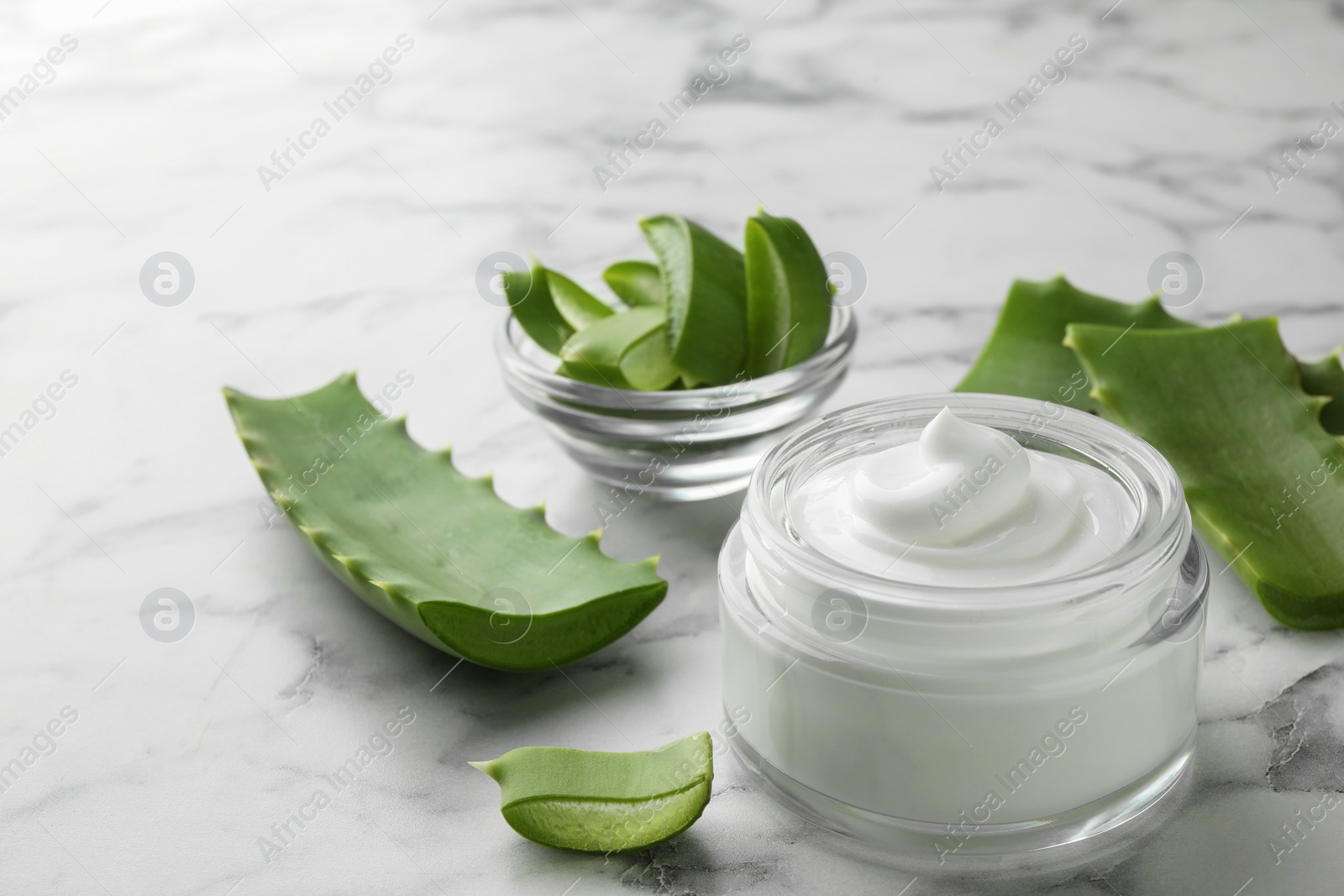 Photo of Jar with cream and cut aloe leaves on white marble table, closeup. Space for text