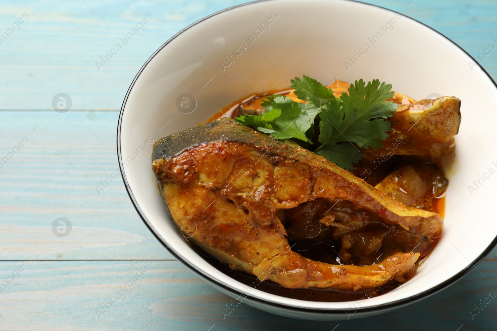 Photo of Tasty fish curry on light blue wooden table, closeup. Indian cuisine