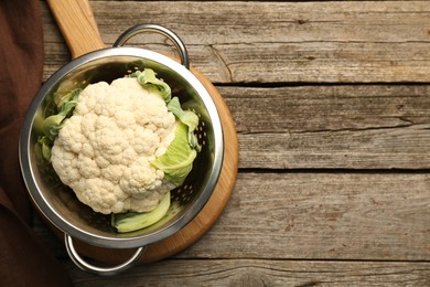 Metal colander with cauliflower on wooden table, top view. Space for text