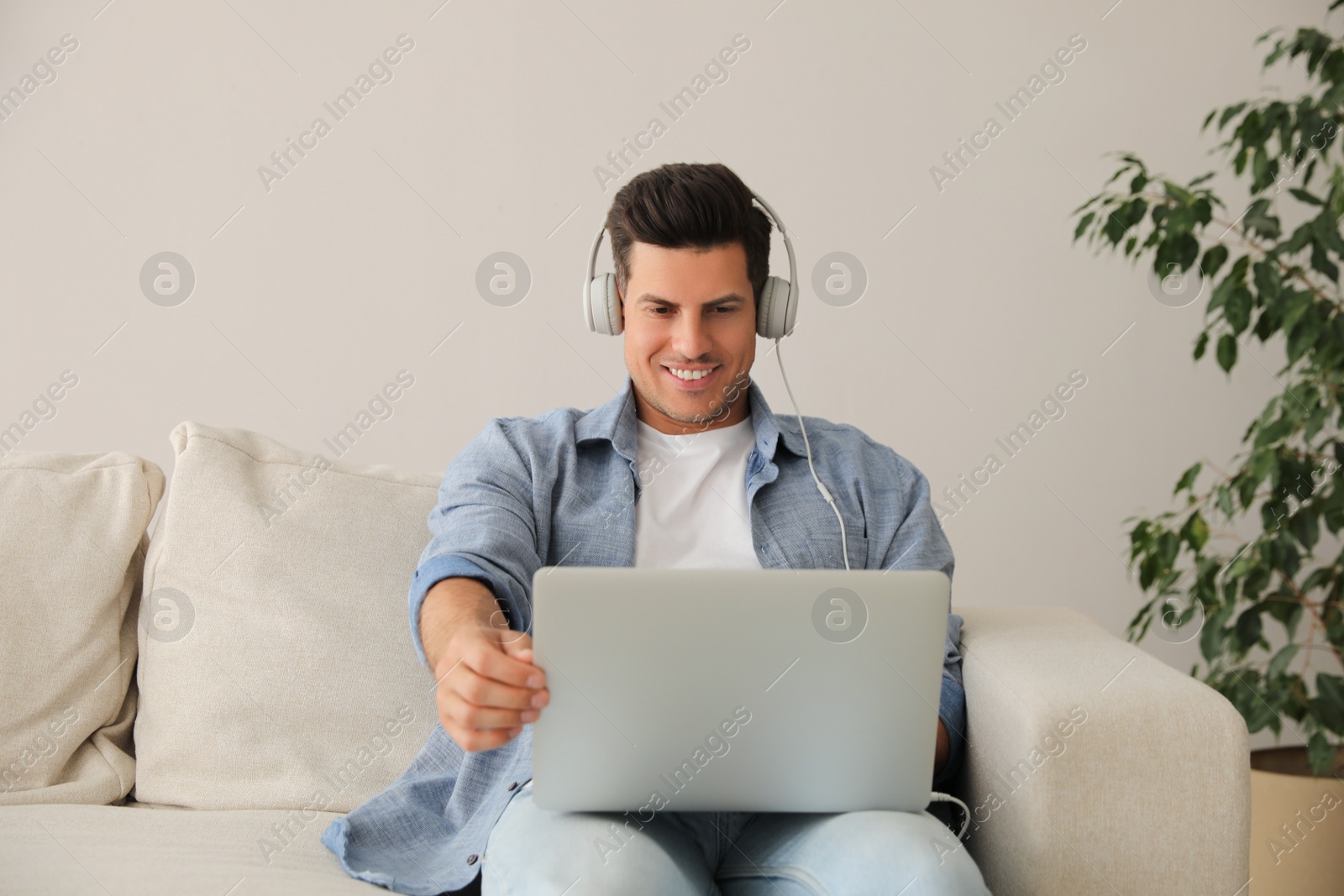 Photo of Man with laptop and headphones sitting on sofa at home