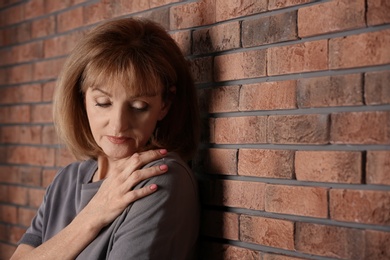 Photo of Senior woman suffering from depression near brick wall
