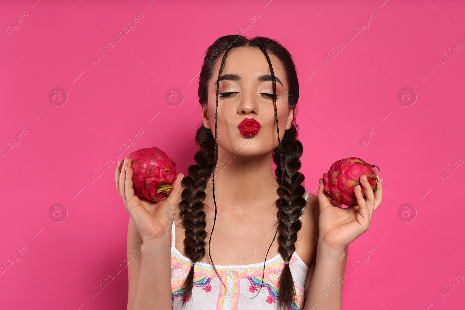 Photo of Young woman with fresh pitahayas on pink background. Exotic fruit