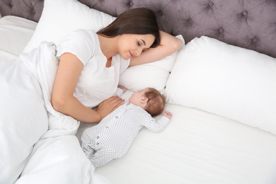 Photo of Woman resting with her sleeping baby on bed
