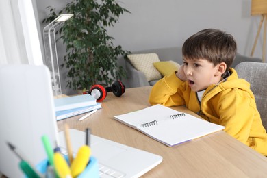 Cute little boy with modern laptop studying online at home. E-learning