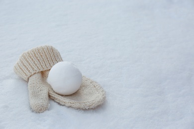 Photo of Knitted mitten and snowball on snow outdoors. Space for text