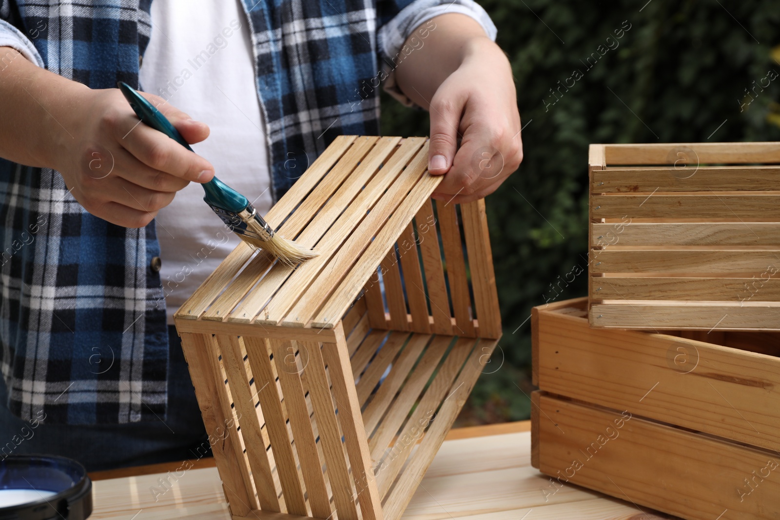 Photo of Man applying varnish onto wooden crate at table outdoors, closeup