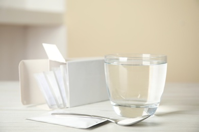 Medicine sachets, glass of water and spoon on white table