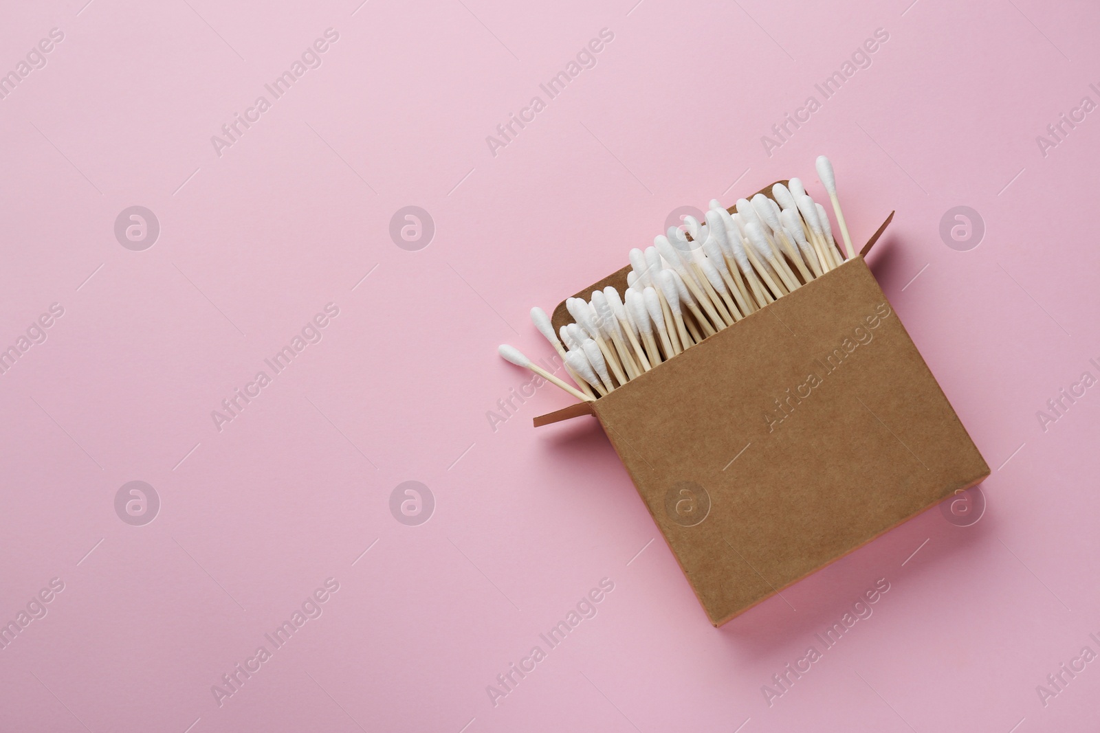 Photo of Cotton buds in cardboard box on pink background, top view. Space for text