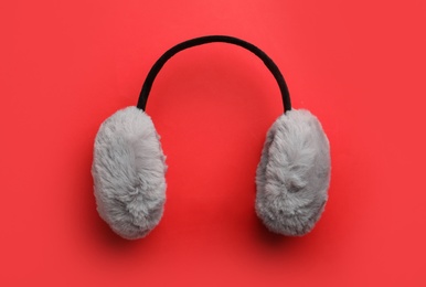 Stylish winter earmuffs on red background, top view