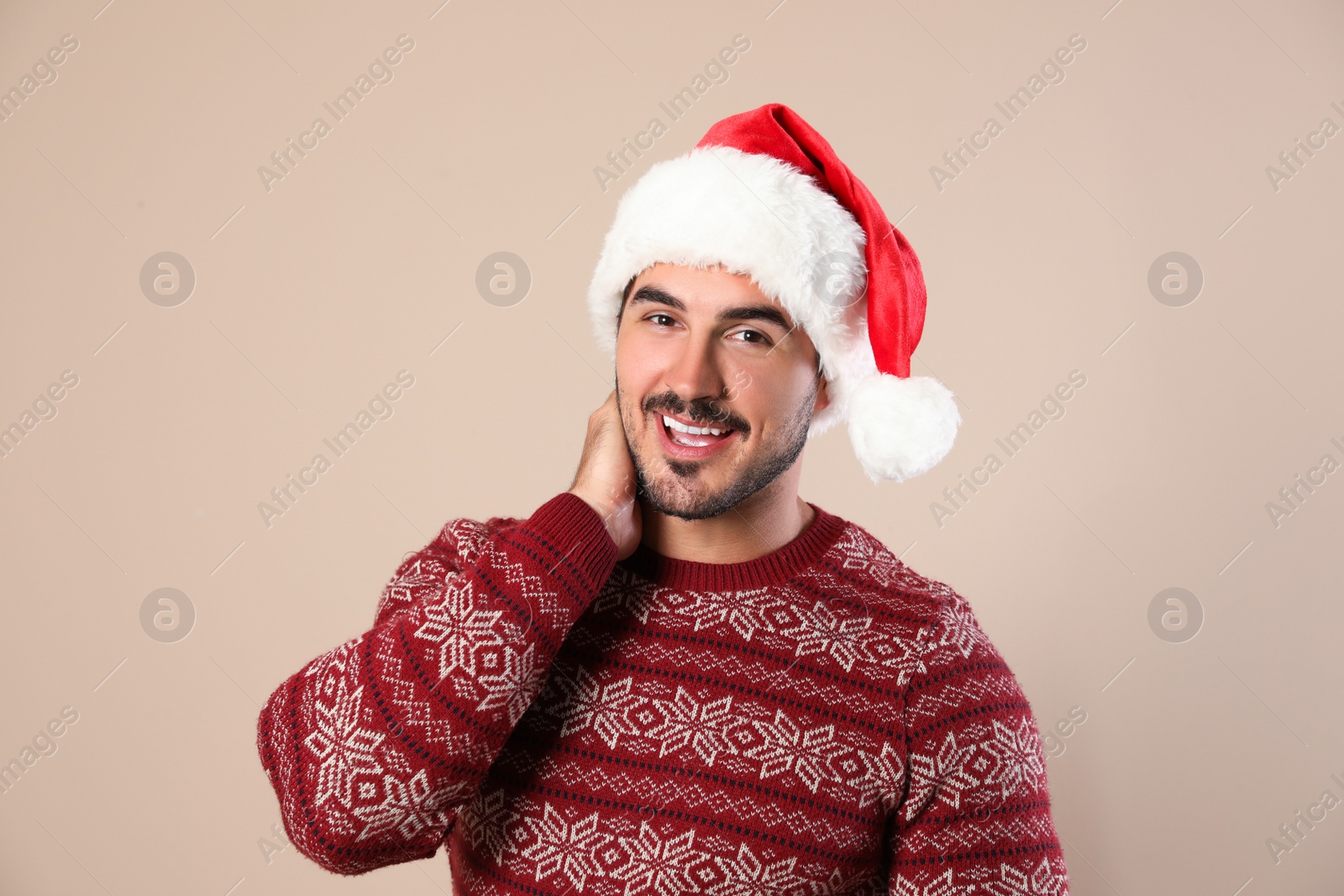 Photo of Portrait of young man in Christmas sweater and Santa hat on beige background