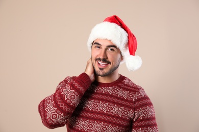 Portrait of young man in Christmas sweater and Santa hat on beige background