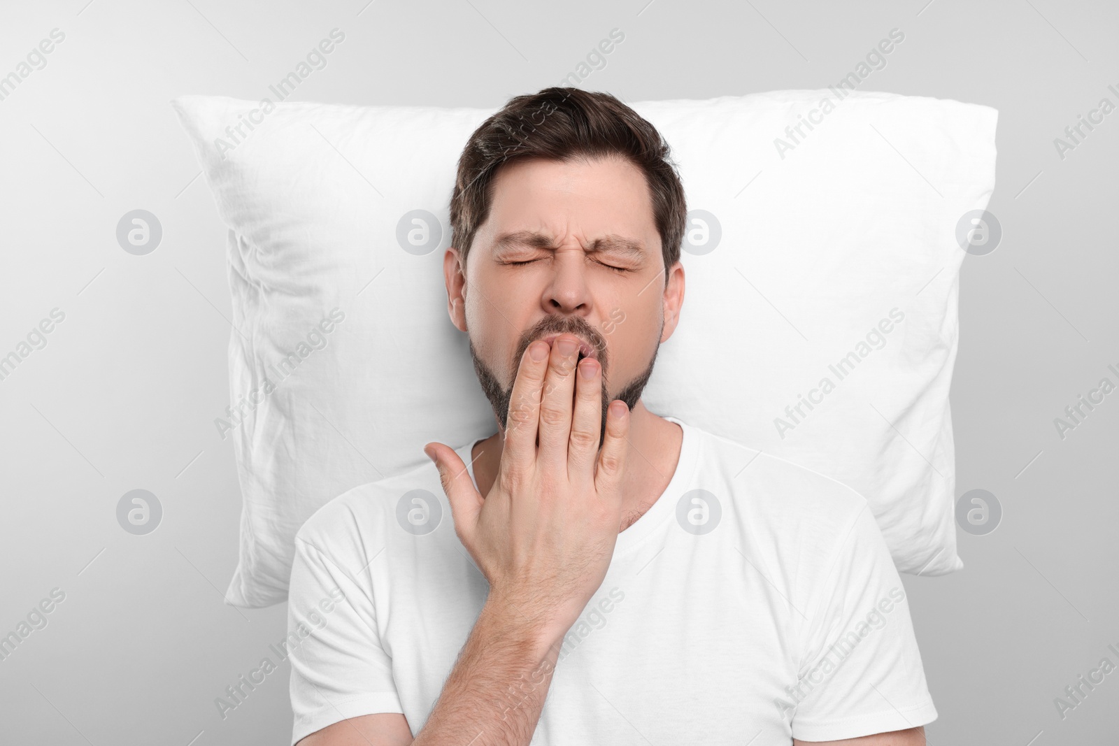 Photo of Tired man with pillow on light grey background. Insomnia problem