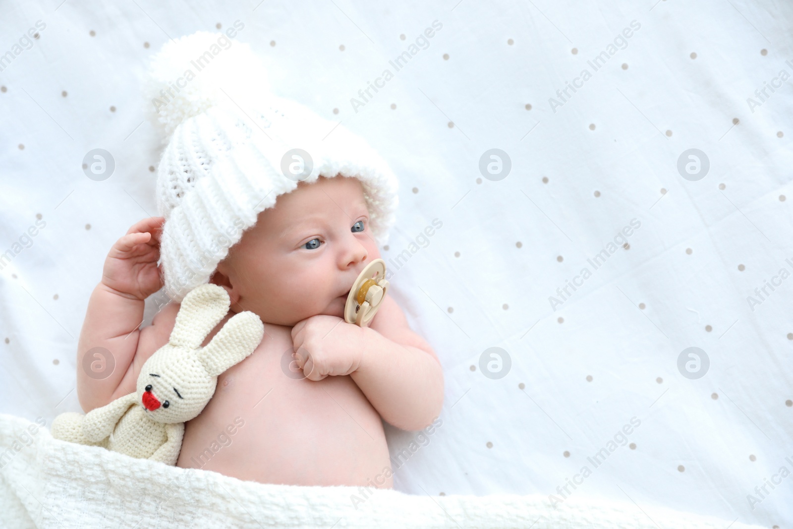 Photo of Cute newborn baby in white knitted hat with toy lying on bed, top view. Space for text
