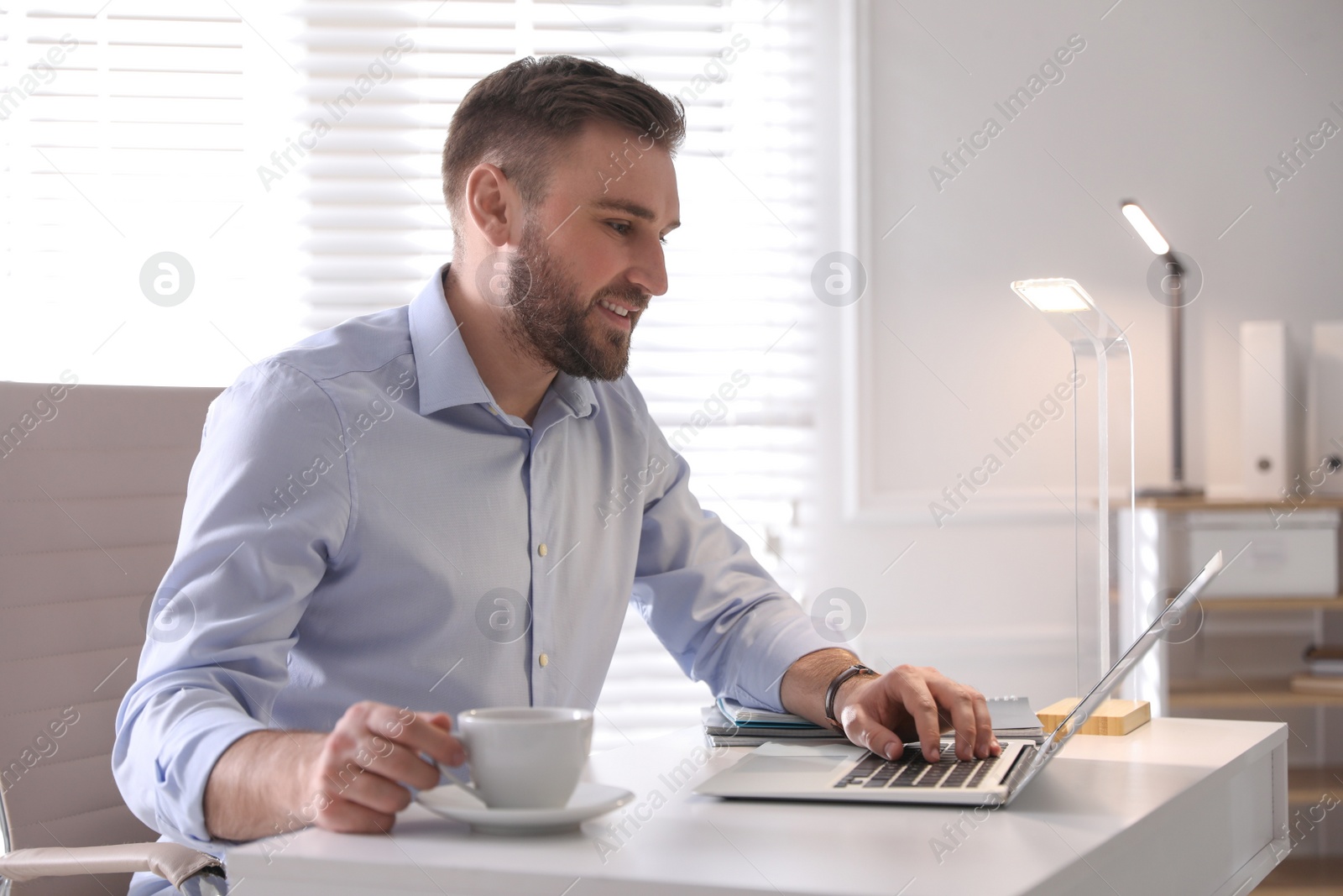 Photo of Young man working on laptop at table in office