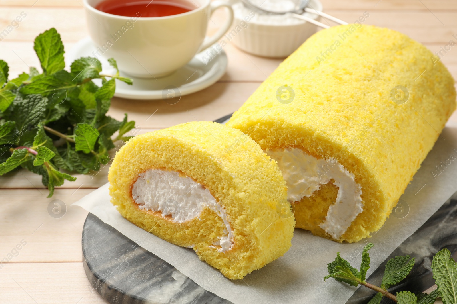 Photo of Delicious cake roll and mint on light wooden table, closeup