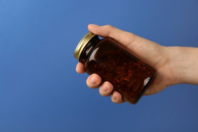 Photo of Woman holding jar with vitamin capsules on blue background, closeup