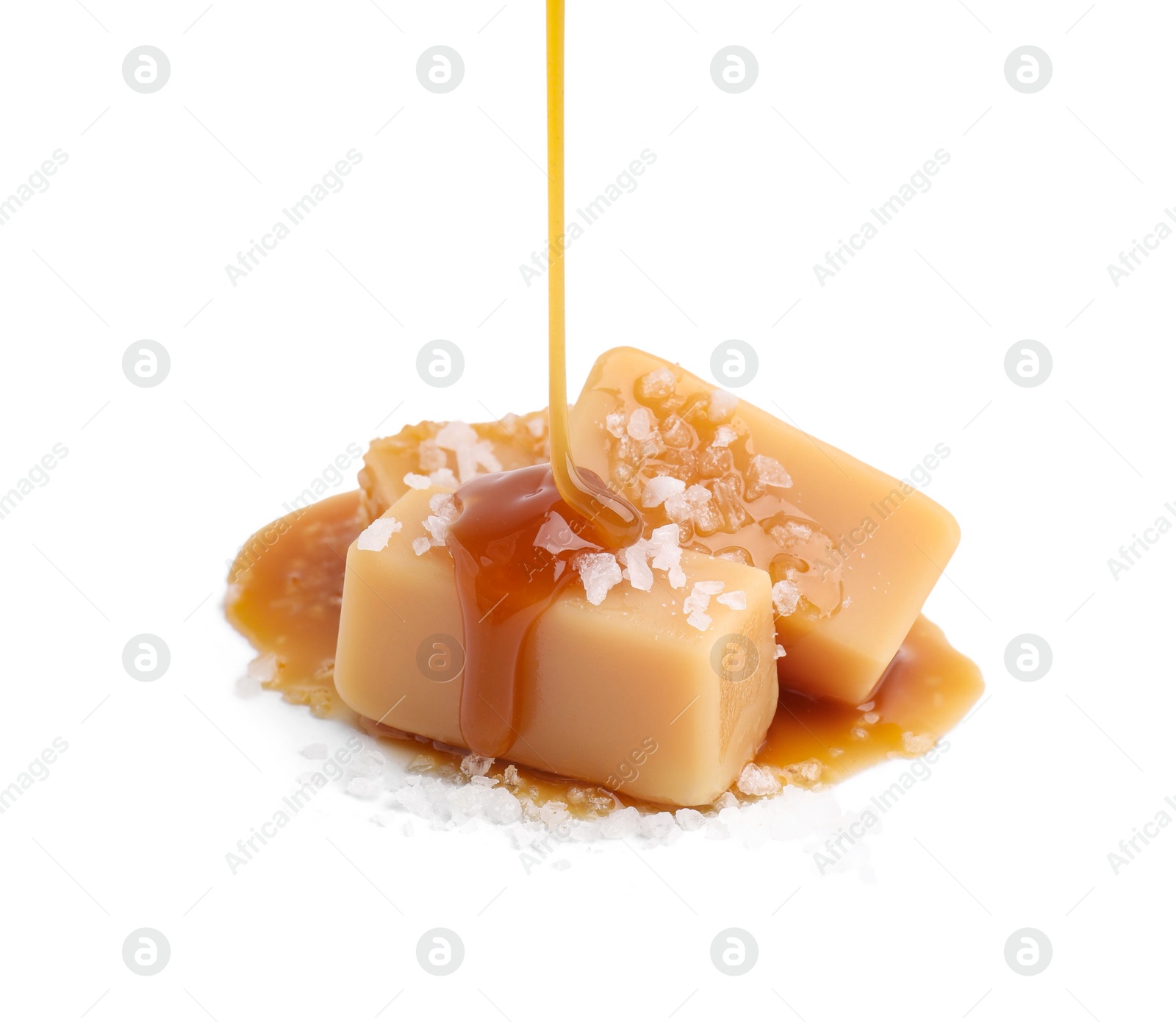 Photo of Pouring delicious salted caramel on candies isolated on white