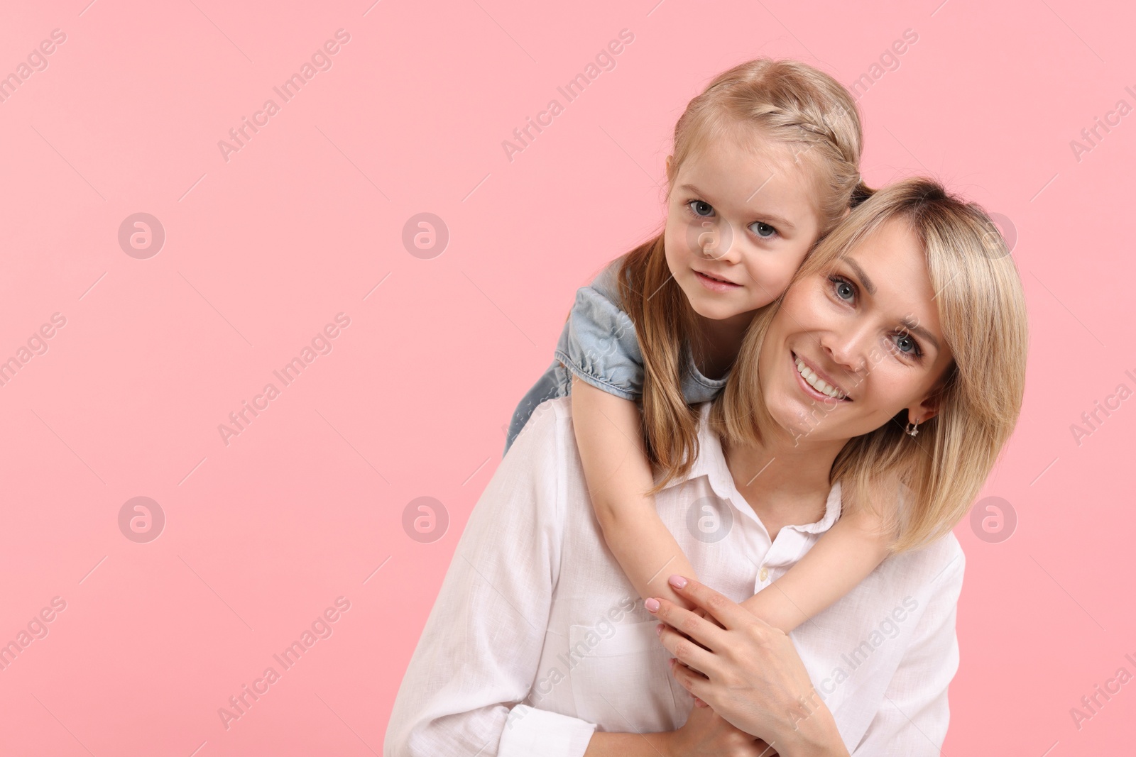 Photo of Daughter hugging her happy mother on pink background. Space for text