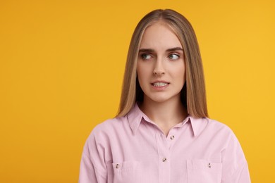 Photo of Portrait of embarrassed young woman on orange background. Space for text