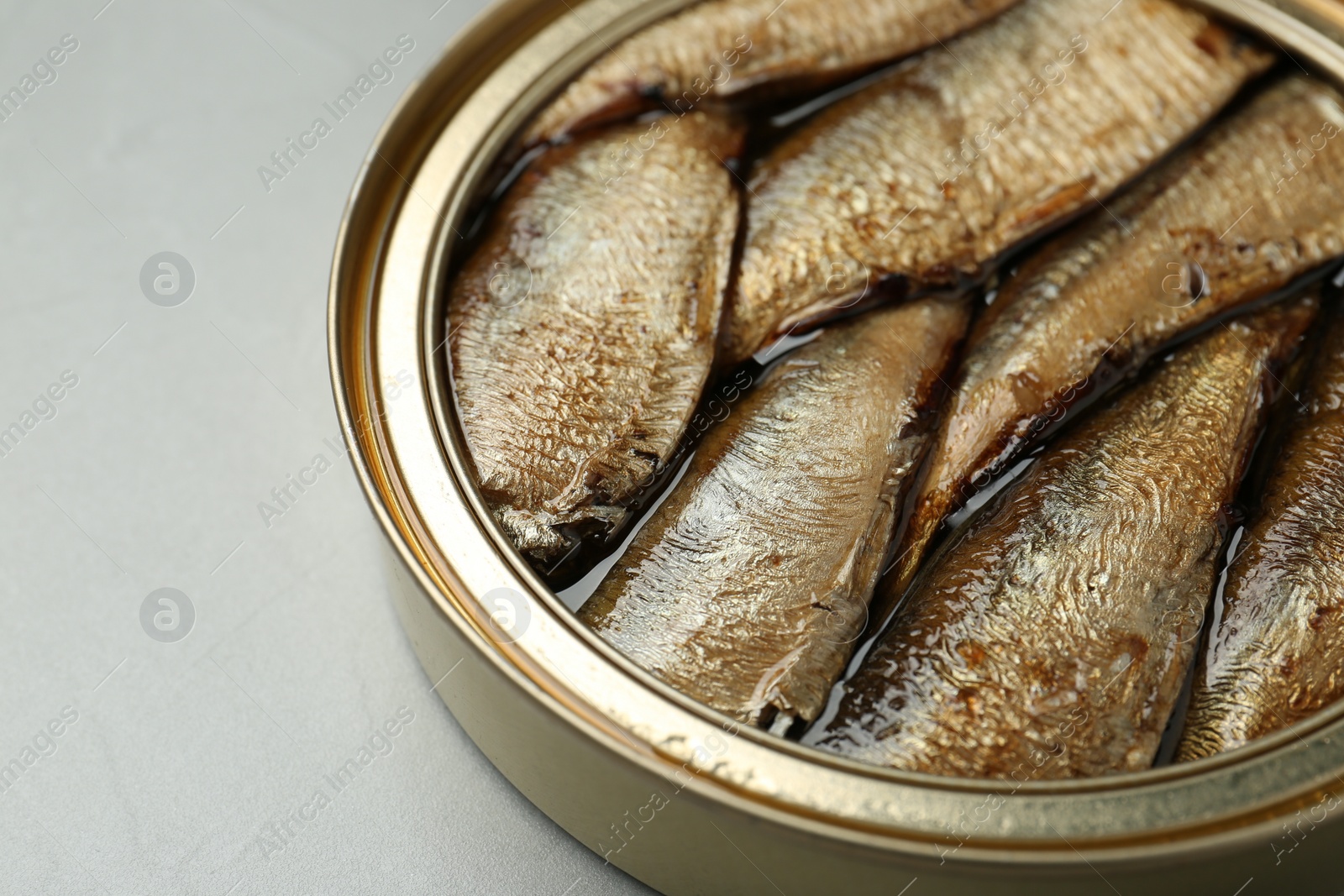 Photo of Open tin can of sprats on light grey table, closeup