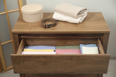 Photo of Chest of drawers with different folded clothes and accessories indoors