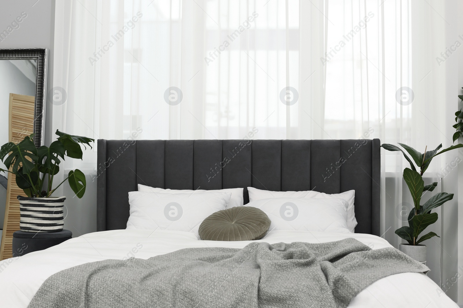 Photo of Large comfortable bed and beautiful houseplants in room. Bedroom interior