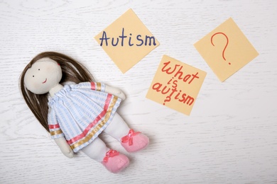 Photo of Notes with words related to autism and doll on light background, top view