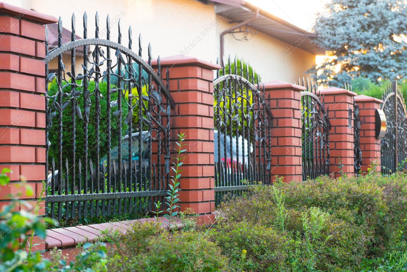 Photo of Bushes and beautiful brick fence with iron railing outdoors