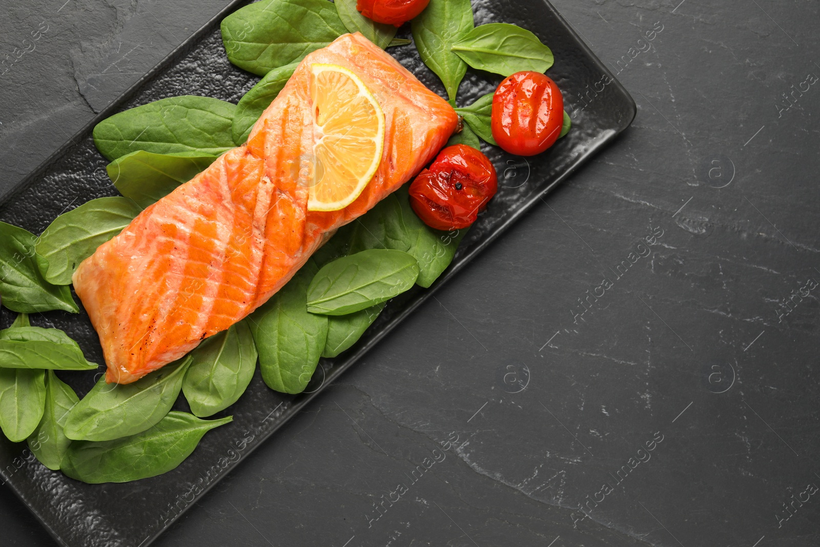 Photo of Tasty grilled salmon with tomatoes, spinach and lemon on black table, top view. Space for text