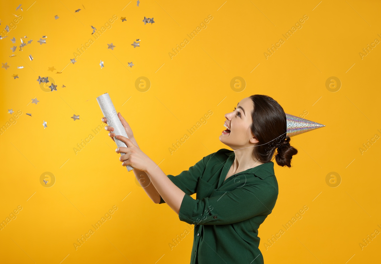 Photo of Young woman blowing up party popper on yellow background