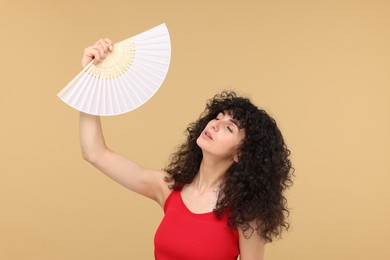 Photo of Woman with hand fan suffering from heat on beige background