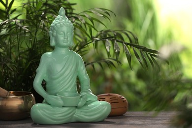 Photo of Buddhism religion. Decorative Buddha statue and singing bowl on wooden table outdoors, space for text