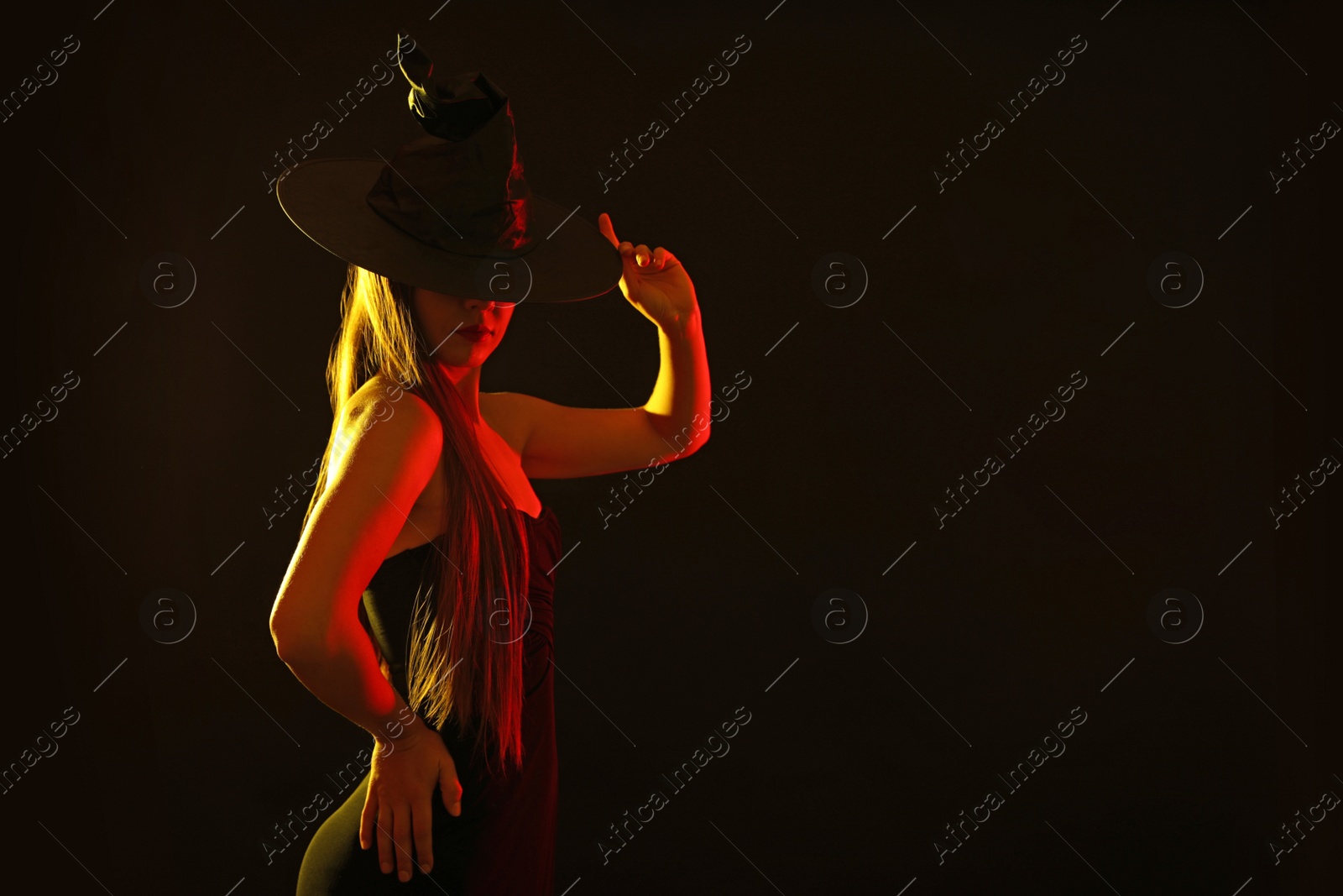 Photo of Young woman wearing witch costume on black background, space for text. Halloween party