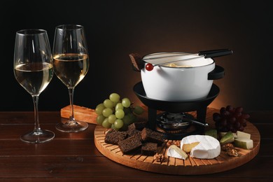 Photo of Forks with pieces of grape, bread, fondue pot with melted cheese, wine and snacks on wooden table