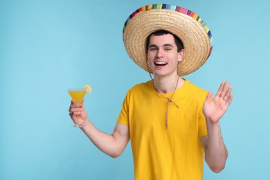 Photo of Young man in Mexican sombrero hat with cocktail on light blue background