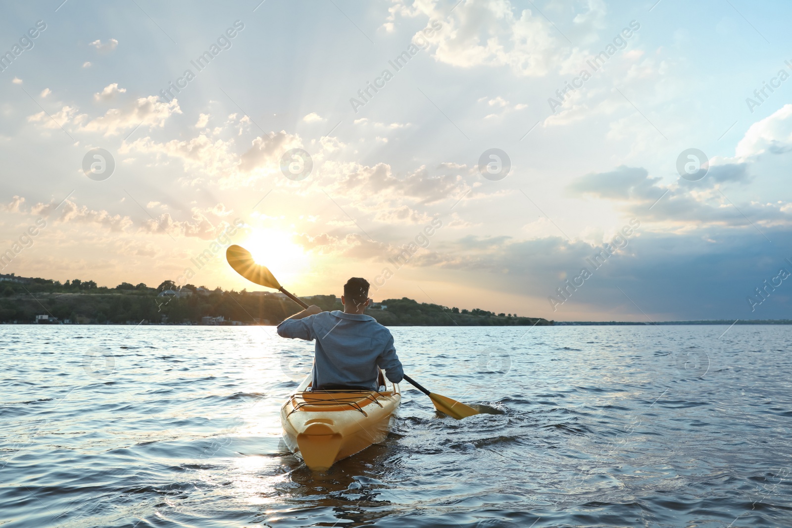 Photo of Man kayaking on river at sunset, back view. Summer activity