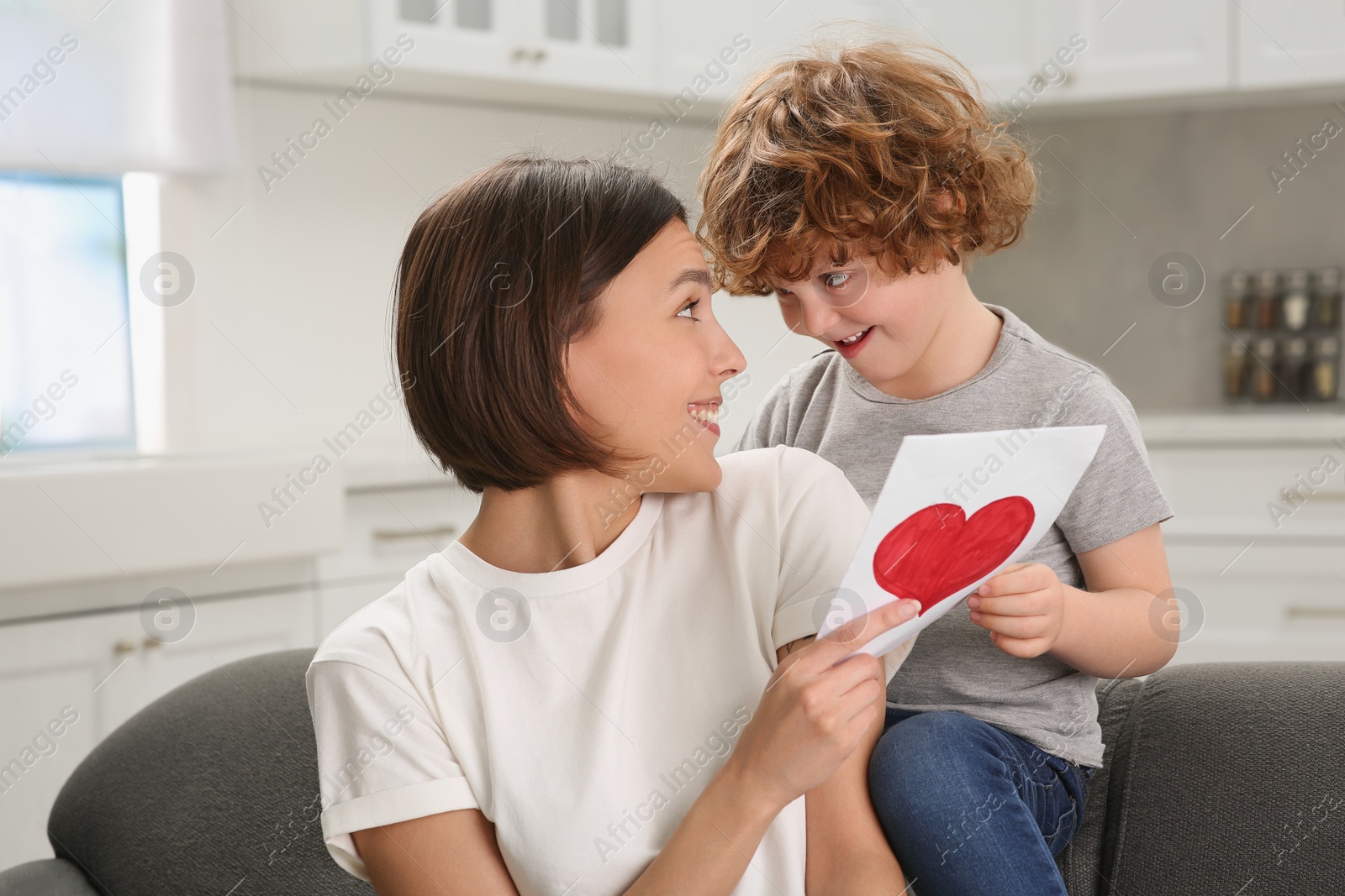 Photo of Little son congratulating his mom with Mother`s day at home. Woman holding greeting card