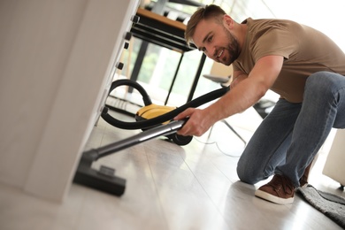 Photo of Young man using vacuum cleaner at home