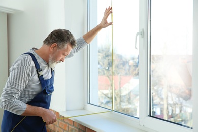 Photo of Service man measuring window for installation indoors