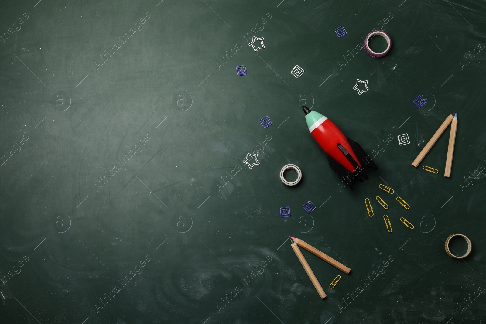 Photo of Bright toy rocket and school supplies on chalkboard, flat lay. Space for text