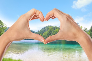 Man making heart with hands near river on sunny day, closeup