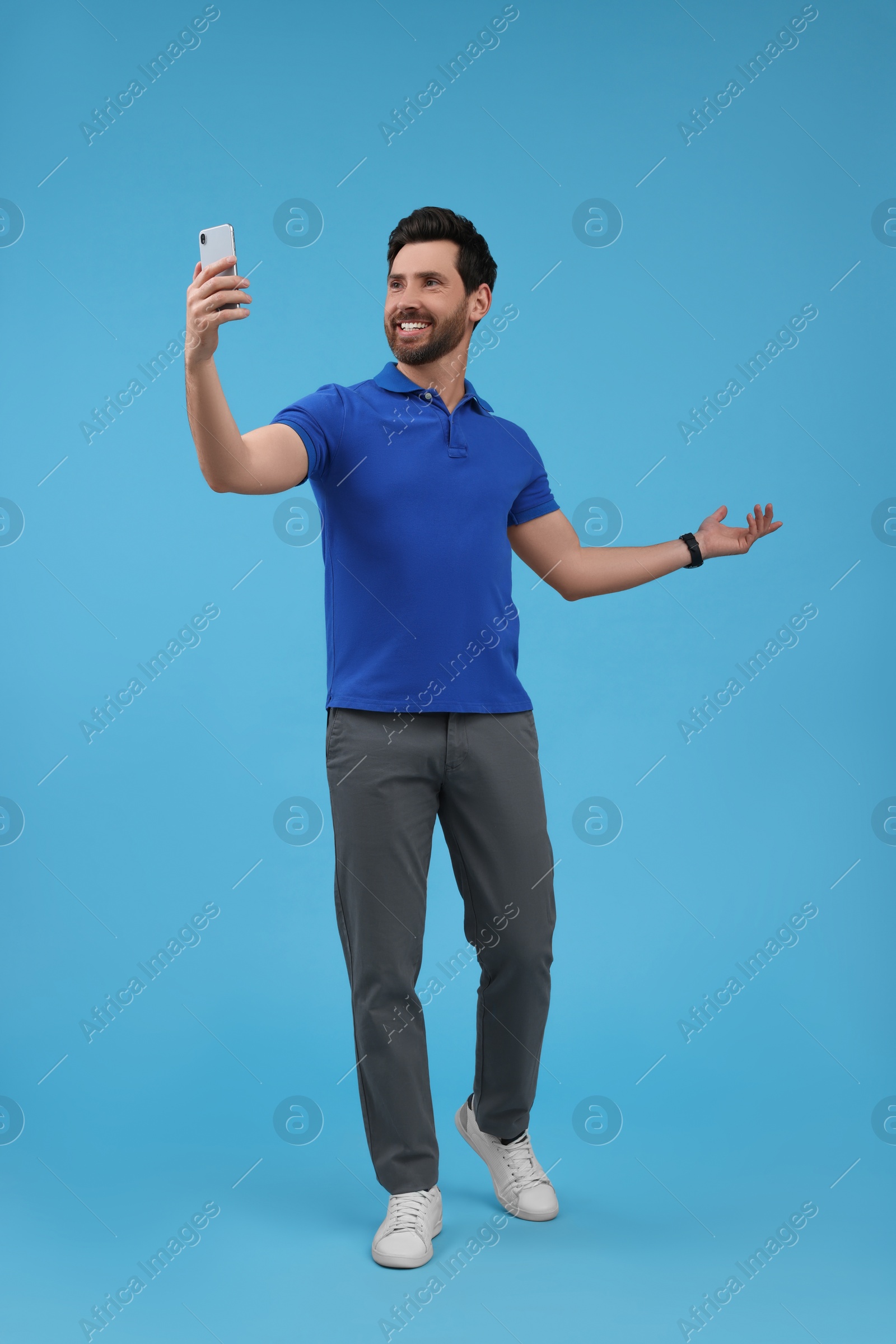 Photo of Smiling man taking selfie with smartphone on light blue background