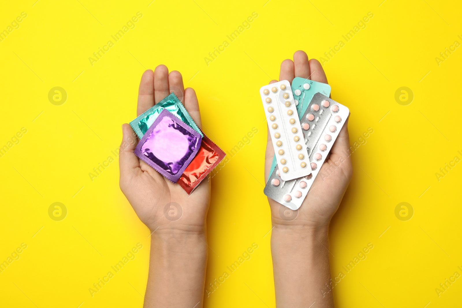 Photo of Woman holding condoms and birth control pills on yellow background, top view. Safe sex