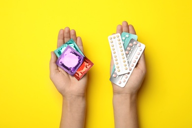 Photo of Woman holding condoms and birth control pills on yellow background, top view. Safe sex