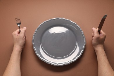 Photo of Man with cutlery and empty plate at brown table, above view
