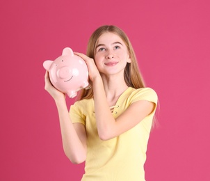Teen girl with piggy bank on color background